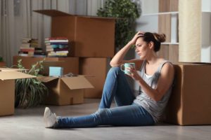 Woman sitting on the floor, holding her head and a mug, surrounded by packages, waiting for New York movers