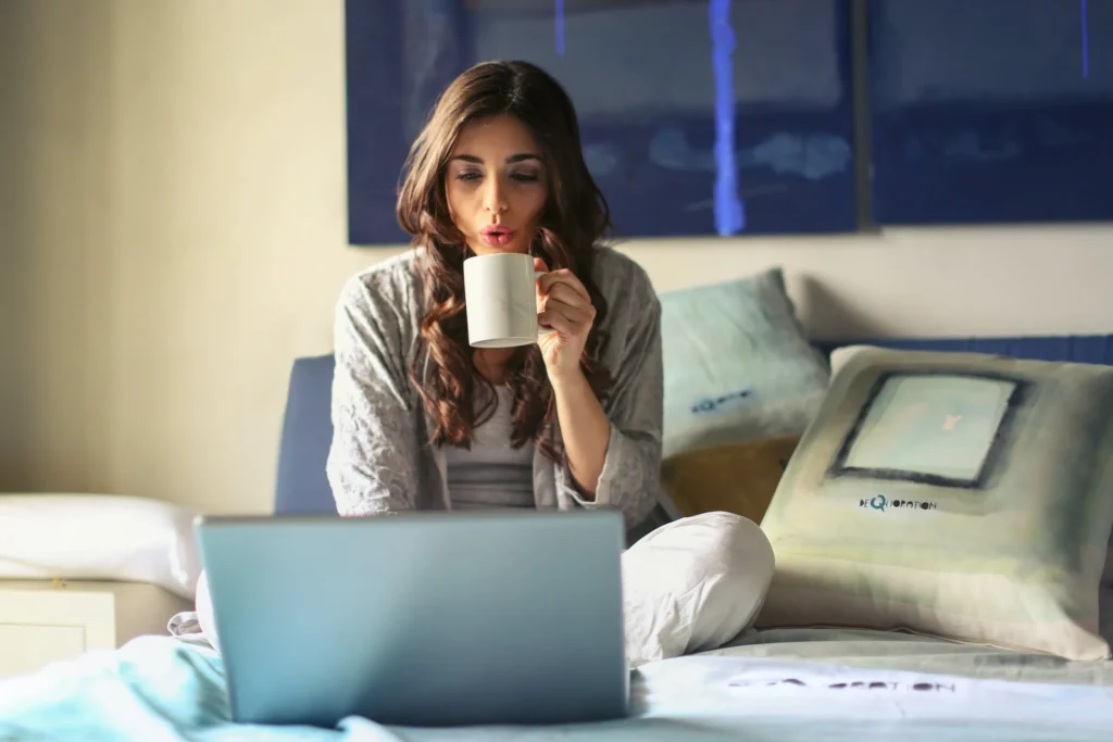 A girl with brown hair sitting on her bad and looking at a laptop